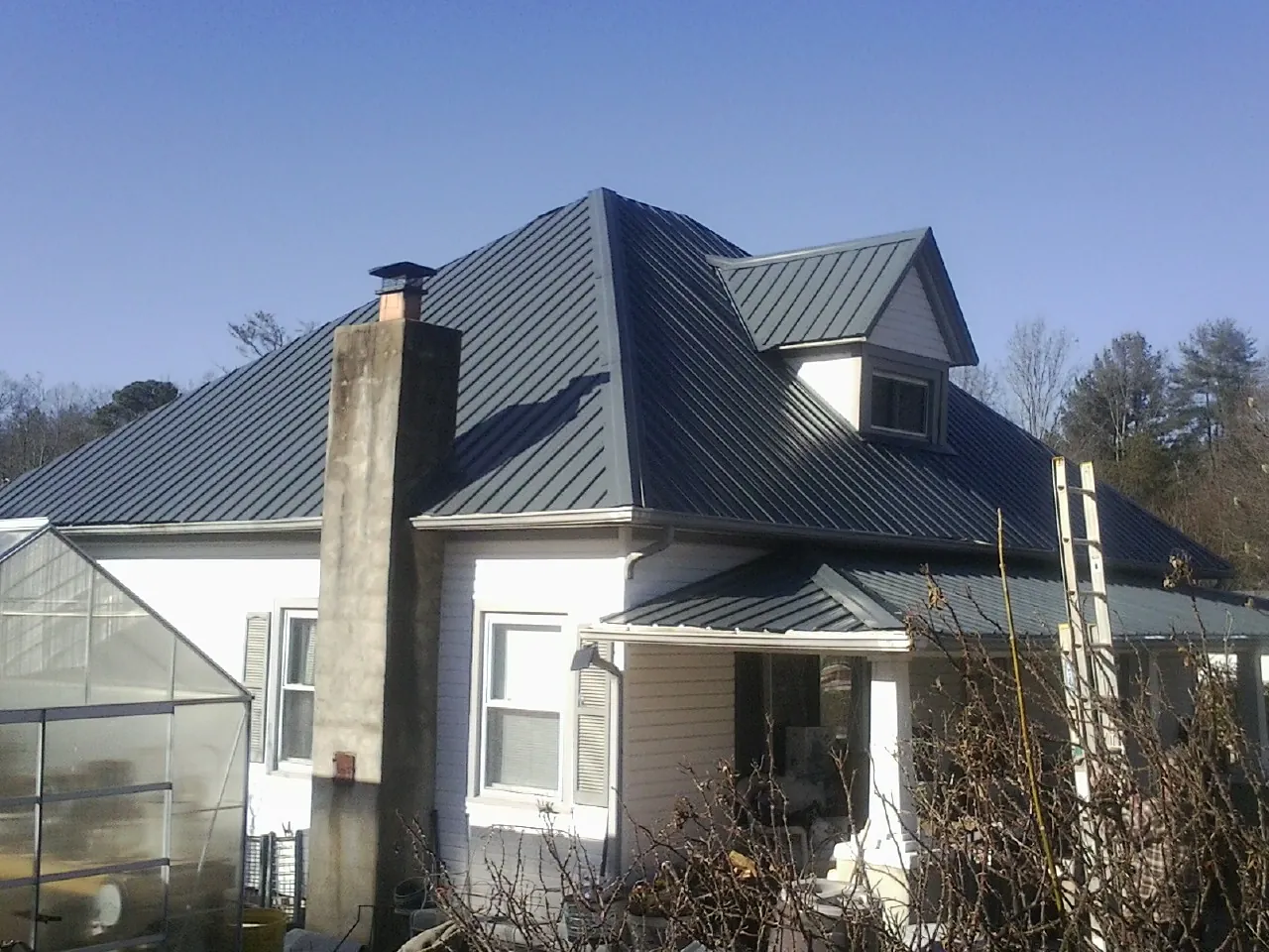 Dark blue standing seam metal roof on a white farmhouse with dormer — Slate & Tile Roof Repair by Roofing Brothers in Hubbard