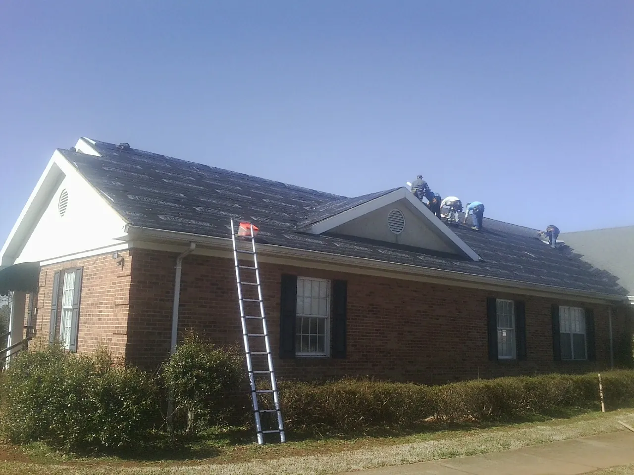 Crew tearing shingles off a brick ranch roof with a ladder set — Emergency Roof Repair work by our crew in Hubbard