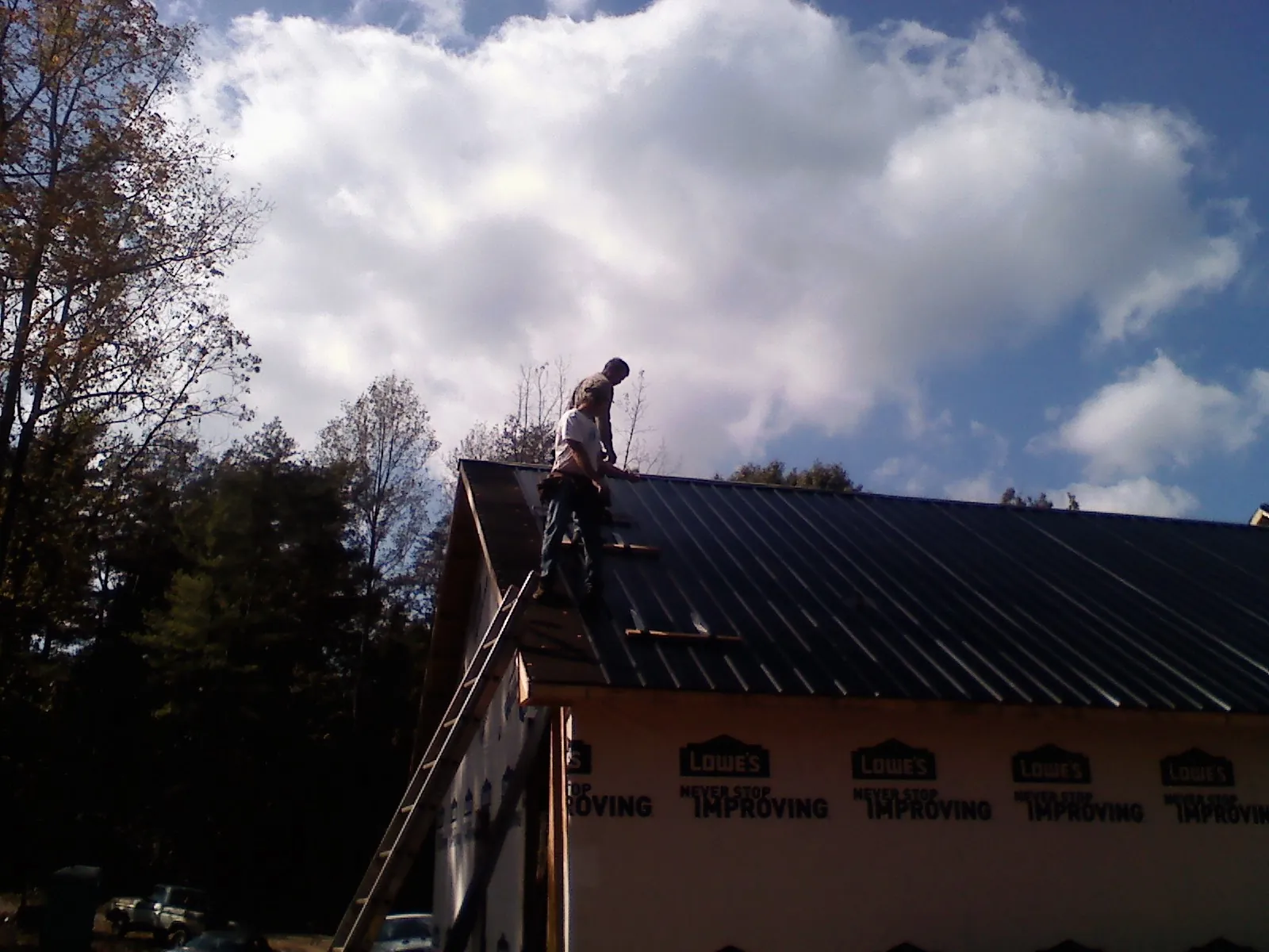 Roofer fastening dark metal panels high against a cloudy sky, from a Roof Inspection job in Hubbard