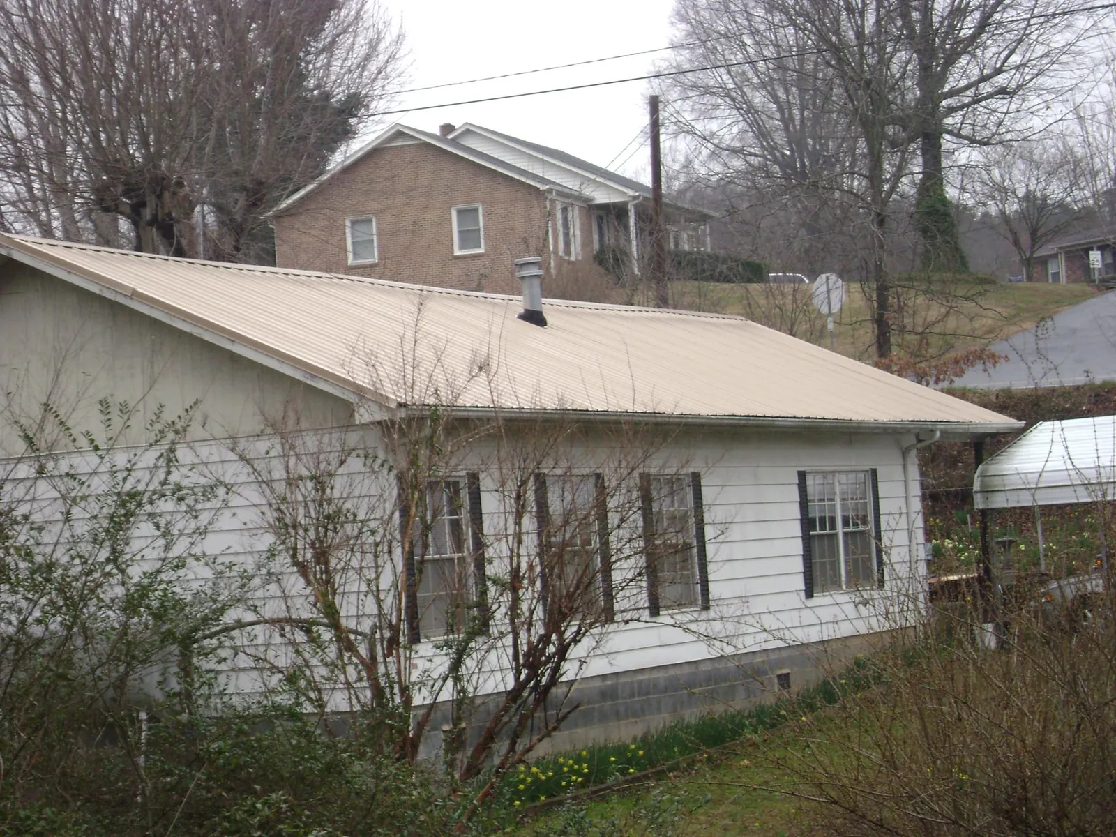 Tan metal roof on a white sided house set into a hillside — Commercial Roofing by Roofing Brothers in Hubbard