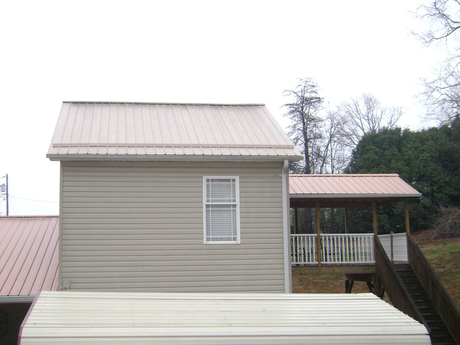 Tan metal roofs on a two story addition and attached porch, from a Roof Replacement job in Hubbard